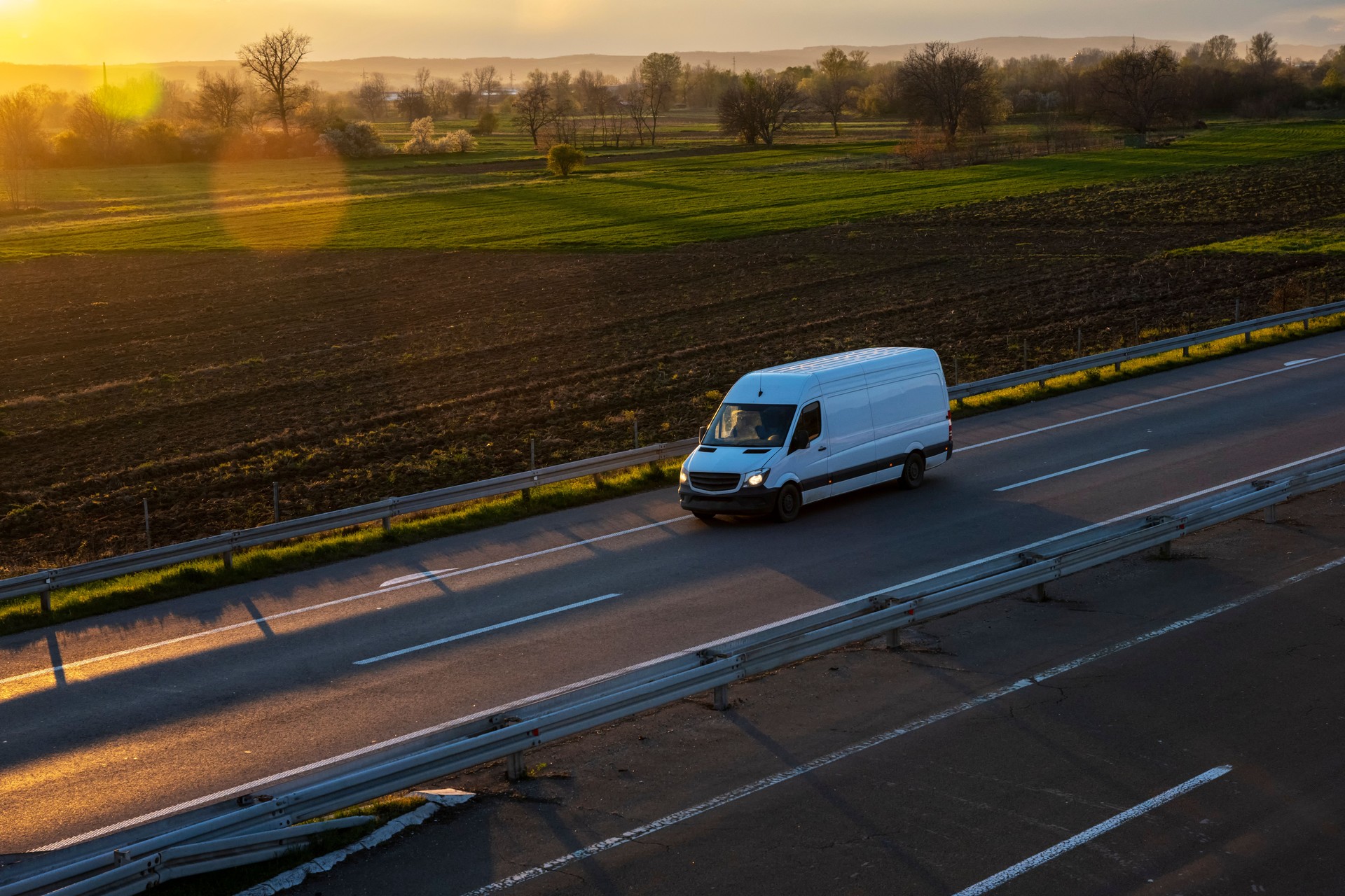 Weißer Lieferwagen auf der Autobahn. Weißer moderner Frachtkurierwagen mit kleiner Lieferung, der sich schnell auf der Autobahnstraße in den städtischen Vorort der Stadt bewegt. Der beste Warentransport der Welt.